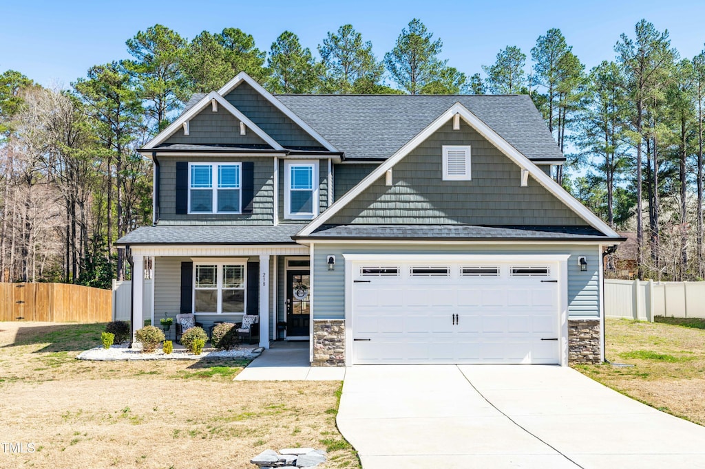 craftsman house with stone siding, driveway, and fence