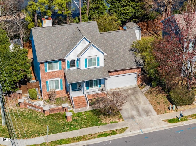 view of front facade with brick siding, fence, a porch, concrete driveway, and a chimney