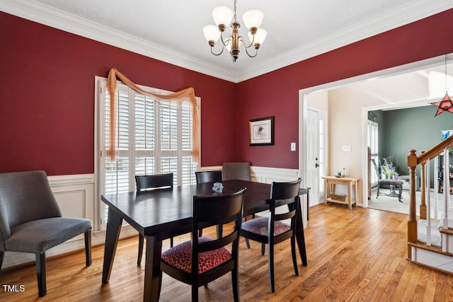 dining space featuring stairs, light wood-style floors, wainscoting, crown molding, and a notable chandelier