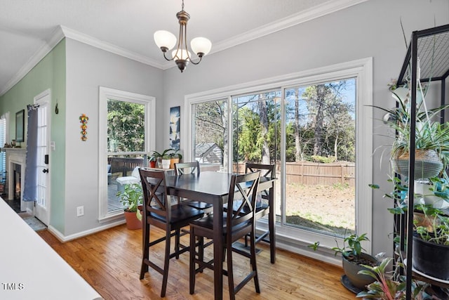 dining area featuring light wood finished floors, baseboards, a lit fireplace, ornamental molding, and a notable chandelier