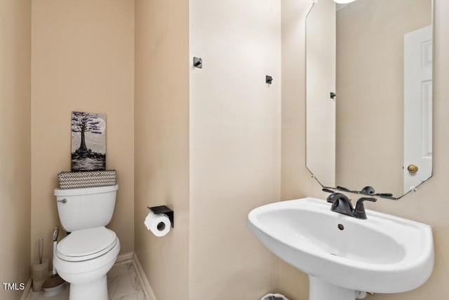 half bathroom featuring toilet, baseboards, and a sink