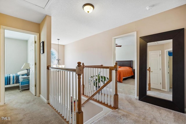 hallway featuring an upstairs landing, a textured ceiling, and carpet floors