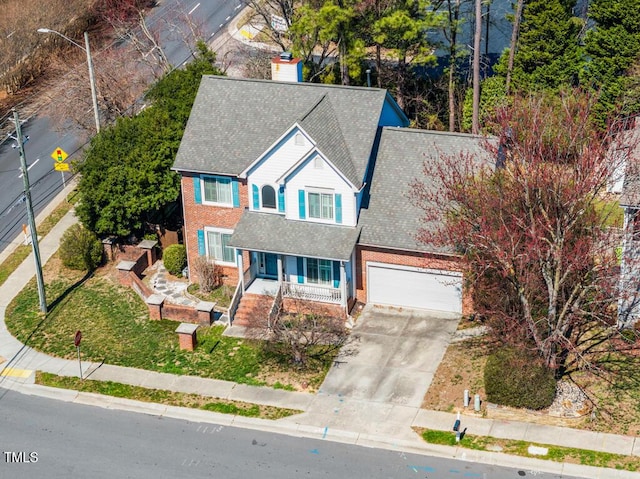 view of front of home with driveway, covered porch, a garage, brick siding, and a chimney