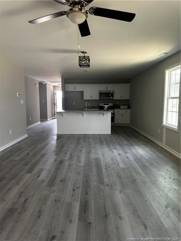 unfurnished living room featuring a sink, baseboards, wood finished floors, and a ceiling fan