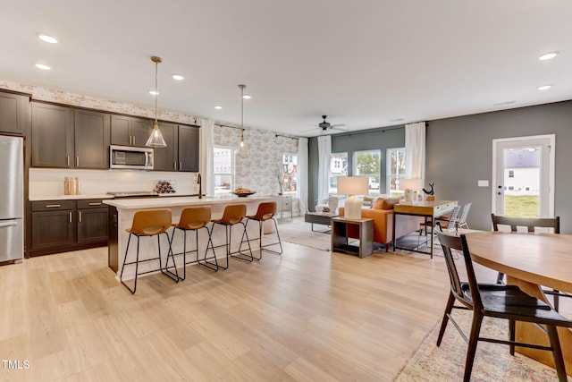 kitchen with light wood-style flooring, an island with sink, stainless steel appliances, light countertops, and a kitchen breakfast bar