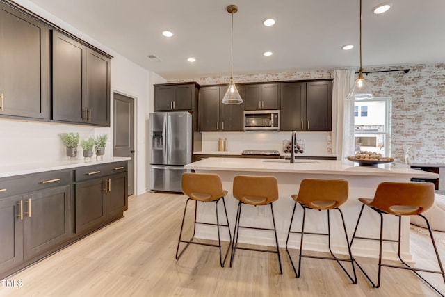 kitchen featuring pendant lighting, a sink, stainless steel appliances, a breakfast bar area, and light wood finished floors