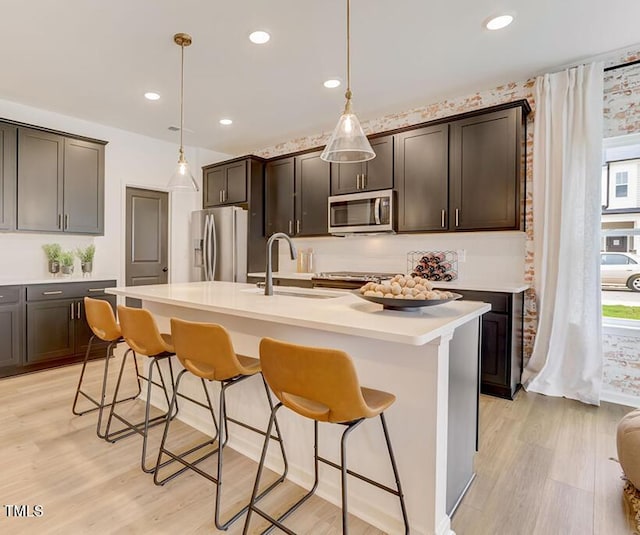 kitchen with a sink, a breakfast bar, light wood finished floors, and stainless steel appliances