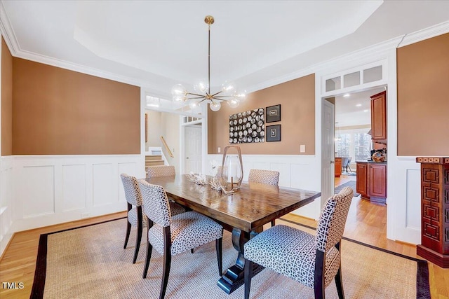 dining space with a wainscoted wall, a notable chandelier, and light wood finished floors