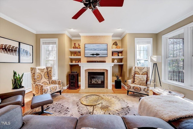 living area featuring a tiled fireplace, crown molding, baseboards, and wood finished floors