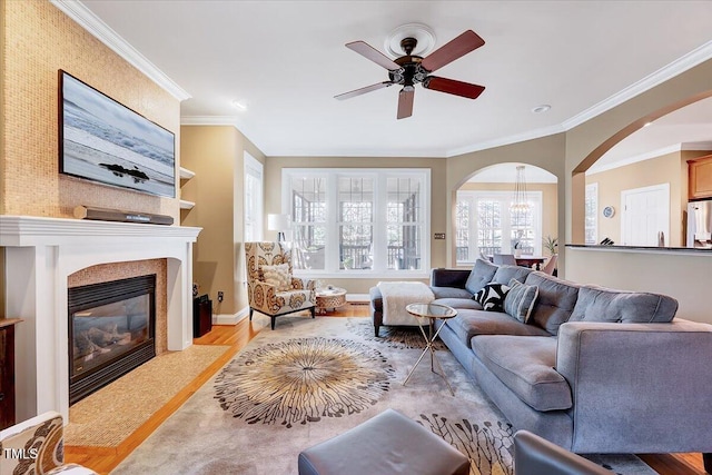 living area with wood finished floors, baseboards, a fireplace with flush hearth, arched walkways, and ornamental molding