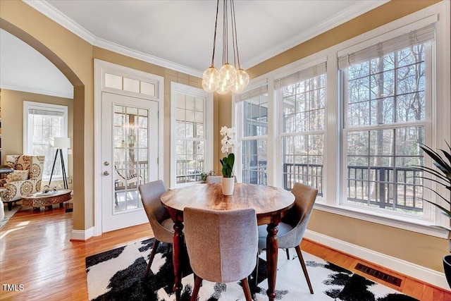 dining room with visible vents, arched walkways, crown molding, and light wood finished floors