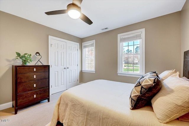 bedroom with visible vents, light carpet, a closet, baseboards, and ceiling fan