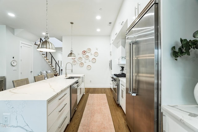 kitchen featuring an island with sink, dark wood-style flooring, a sink, white cabinets, and premium appliances