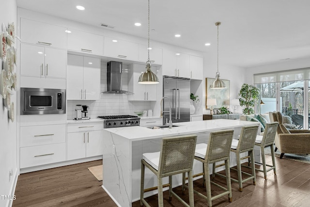 kitchen featuring built in appliances, dark wood-type flooring, modern cabinets, and wall chimney range hood