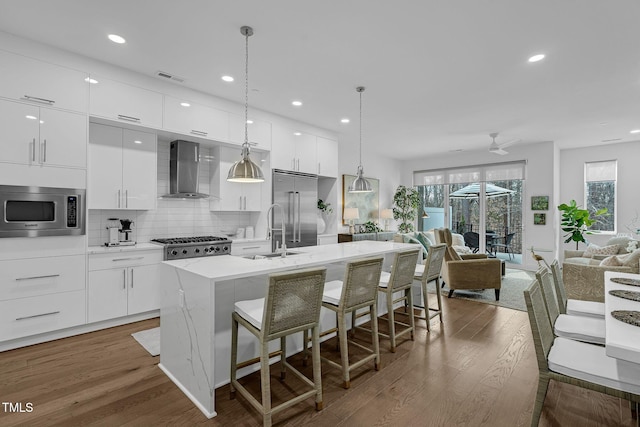 kitchen featuring built in appliances, a kitchen breakfast bar, modern cabinets, and wall chimney range hood