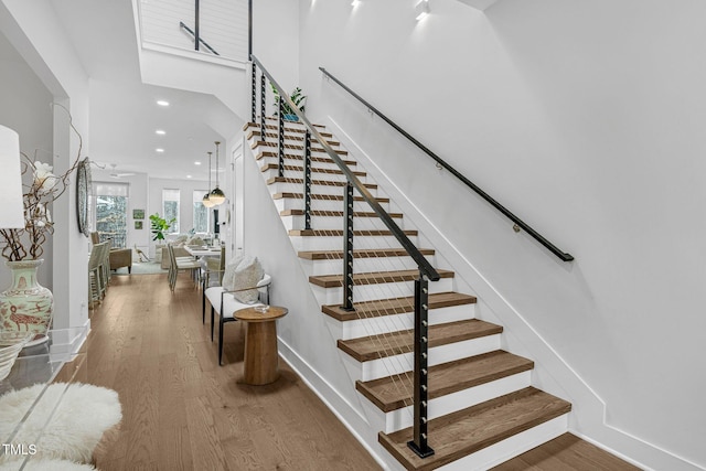 stairway with recessed lighting, baseboards, a high ceiling, and wood finished floors