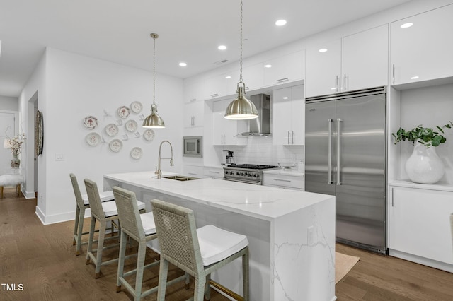 kitchen with a sink, white cabinetry, wall chimney range hood, built in appliances, and dark wood-style flooring