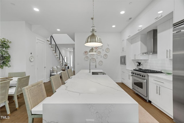 kitchen featuring a kitchen island with sink, a sink, white cabinetry, wall chimney range hood, and high quality appliances