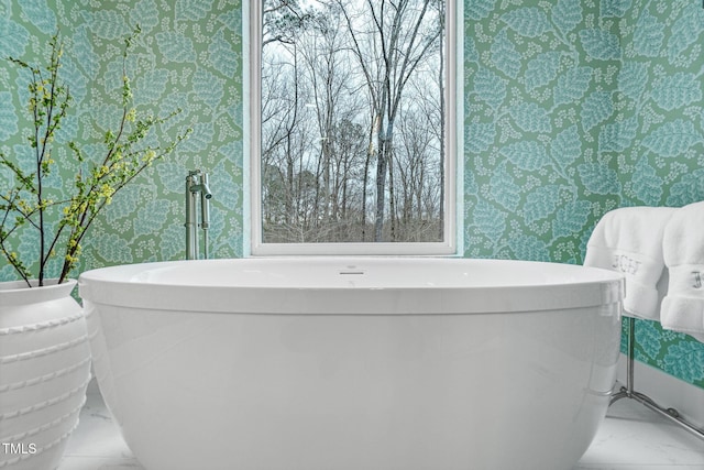 bathroom with marble finish floor, wallpapered walls, and a freestanding tub