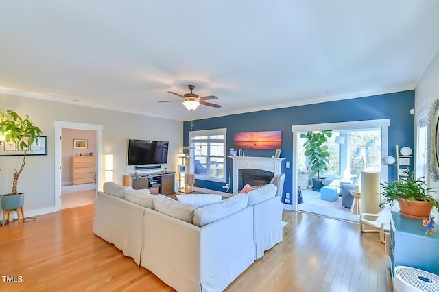 living area with baseboards, a fireplace, a ceiling fan, and light wood-style floors