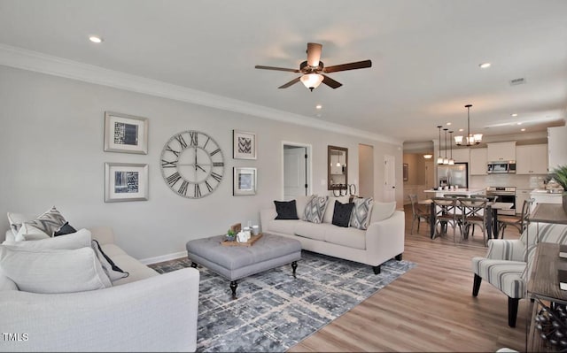 living area with ceiling fan with notable chandelier, light wood-style floors, visible vents, and ornamental molding