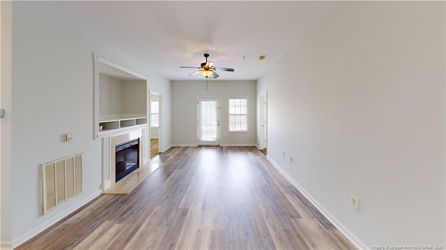 unfurnished living room with a ceiling fan, wood finished floors, visible vents, baseboards, and a high end fireplace