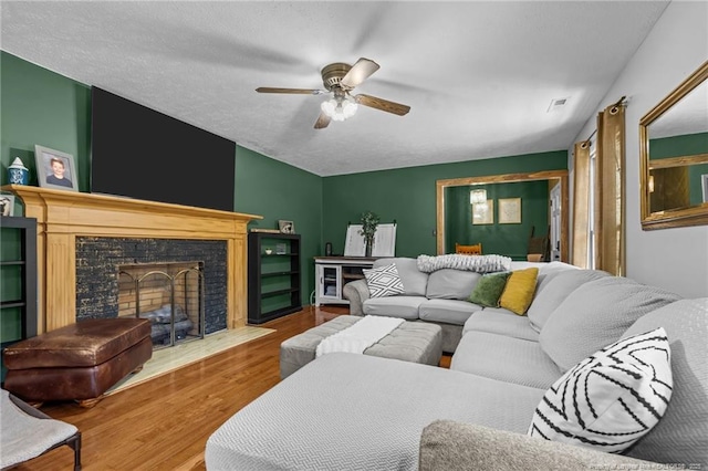 living area with visible vents, ceiling fan, a tiled fireplace, wood finished floors, and a textured ceiling