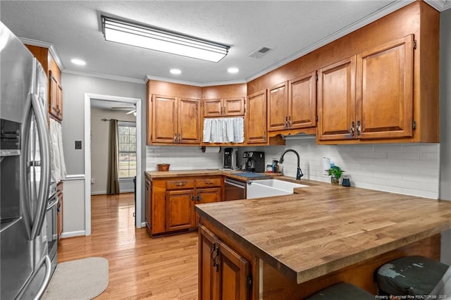 kitchen with brown cabinetry, a peninsula, a sink, butcher block countertops, and stainless steel appliances