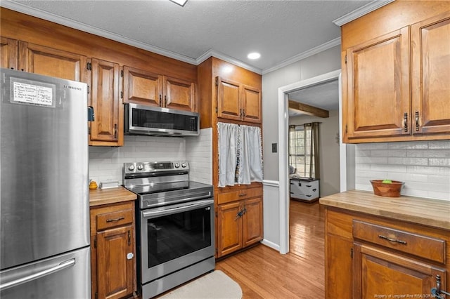 kitchen with brown cabinets, stainless steel appliances, light wood-style flooring, and ornamental molding