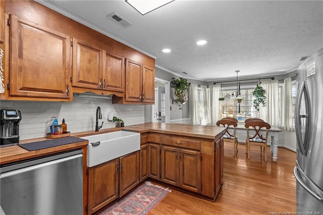 kitchen featuring visible vents, brown cabinets, a sink, stainless steel appliances, and a peninsula