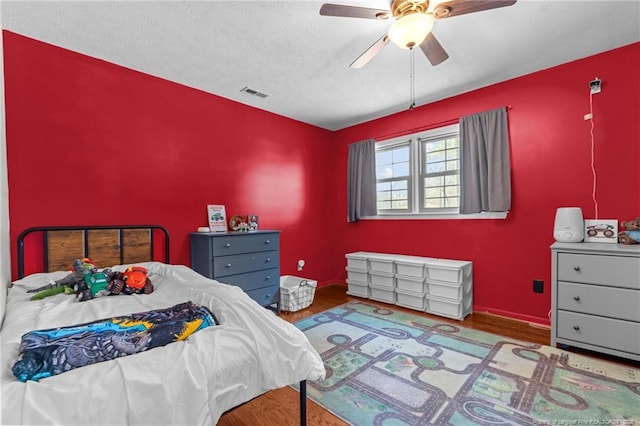 bedroom with a ceiling fan, wood finished floors, visible vents, and a textured ceiling