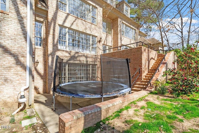 back of property featuring stairway, a trampoline, and brick siding