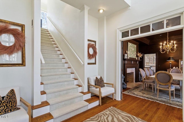 stairway with a chandelier, wood finished floors, and crown molding