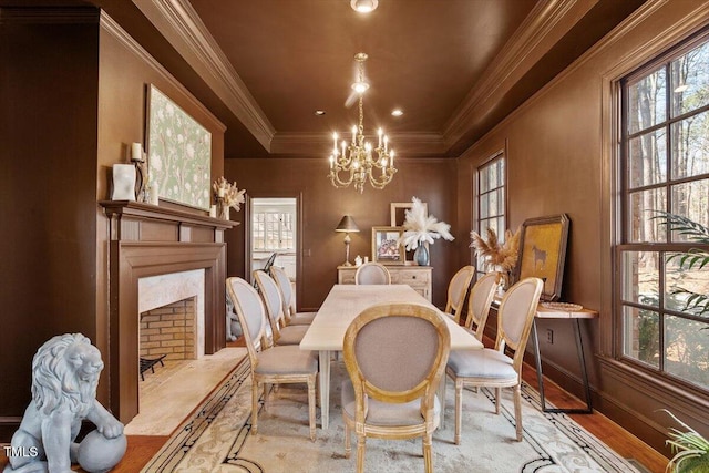 dining space featuring baseboards, a chandelier, a premium fireplace, ornamental molding, and wood finished floors