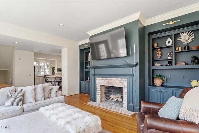 living area featuring built in features, wood finished floors, baseboards, a fireplace, and crown molding