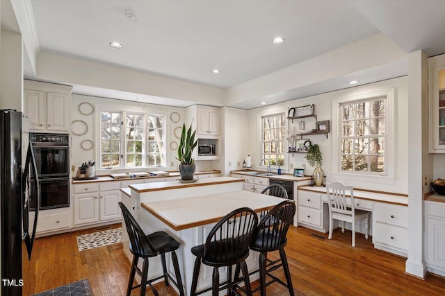 kitchen featuring a kitchen island, dark wood finished floors, a kitchen bar, black appliances, and a sink