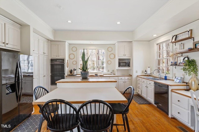 kitchen featuring black appliances, light wood-style flooring, a sink, a center island, and light countertops