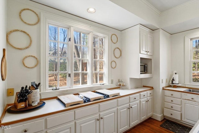 kitchen featuring dark wood finished floors, light countertops, ornamental molding, white cabinetry, and a sink