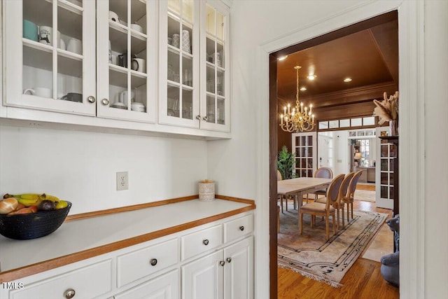 kitchen featuring glass insert cabinets, light countertops, wood finished floors, a notable chandelier, and white cabinetry