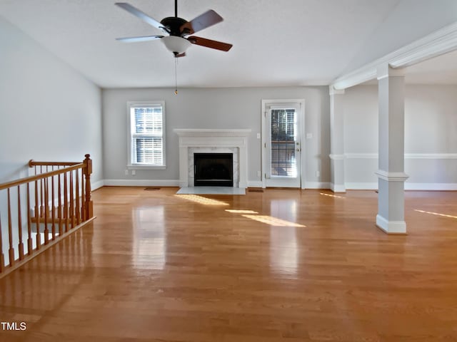 unfurnished living room with wood finished floors, baseboards, a premium fireplace, lofted ceiling, and decorative columns