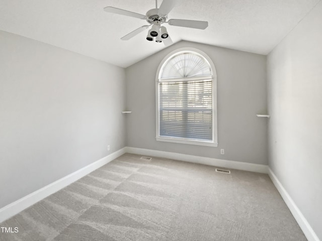 empty room with visible vents, lofted ceiling, a ceiling fan, carpet floors, and baseboards