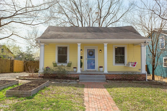 bungalow-style house with a garden, covered porch, roof with shingles, and fence