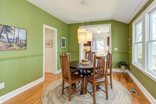 dining space featuring visible vents, baseboards, lofted ceiling, and light wood-style flooring