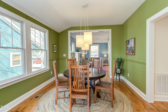 dining space with vaulted ceiling, baseboards, visible vents, and light wood finished floors