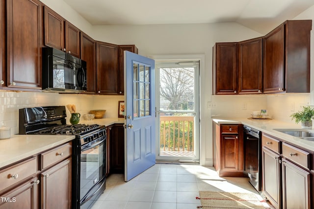 kitchen featuring light countertops, lofted ceiling, light tile patterned floors, decorative backsplash, and black appliances