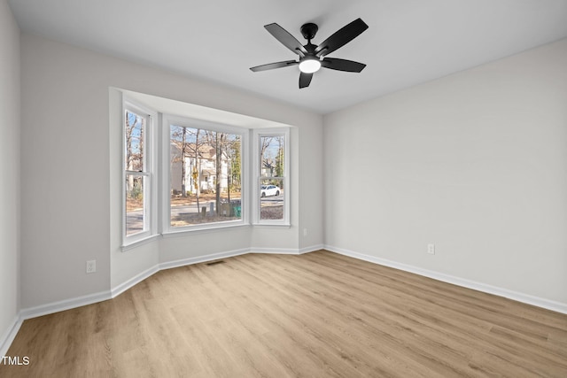 empty room featuring a ceiling fan, wood finished floors, visible vents, and baseboards