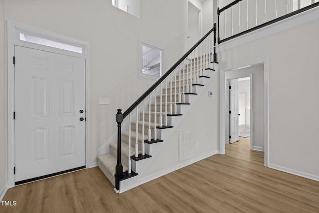 entrance foyer featuring visible vents, wood finished floors, stairway, baseboards, and a towering ceiling