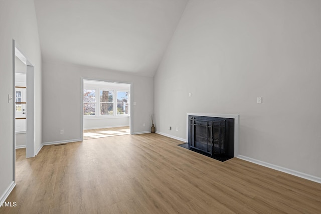 unfurnished living room with baseboards, a fireplace with flush hearth, high vaulted ceiling, and wood finished floors