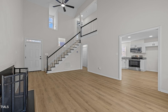 unfurnished living room with stairway, a ceiling fan, baseboards, visible vents, and light wood finished floors