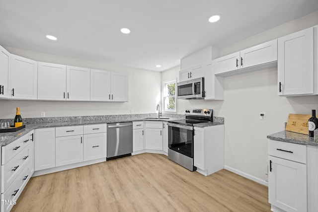 kitchen with a sink, appliances with stainless steel finishes, white cabinets, light wood finished floors, and stone counters